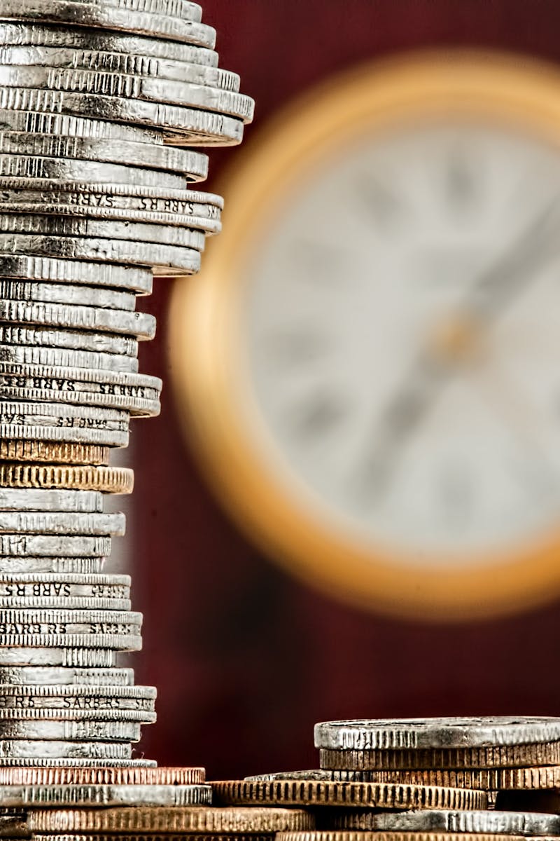 A close-up image of stacked coins with a blurred clock, symbolizing time and money relationship.