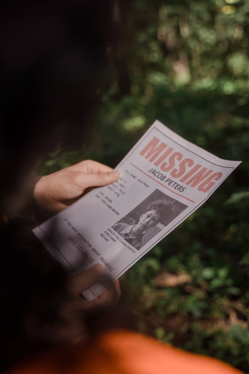 Close-up of a missing person poster being held in a forest environment.