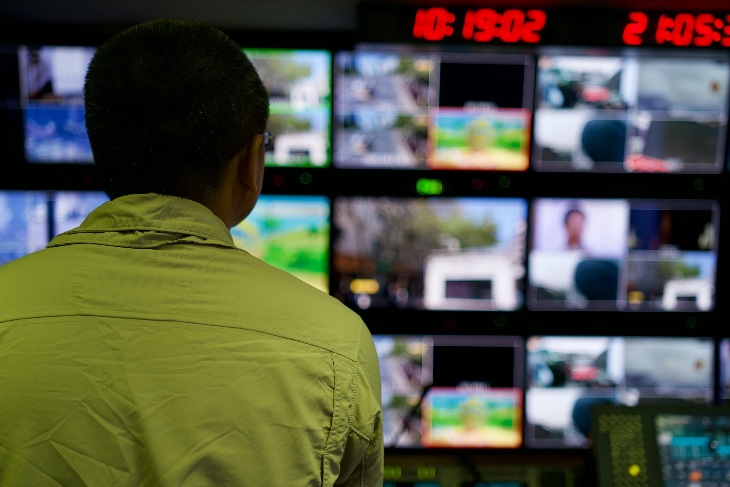 Man in a control room overseeing multiple monitors displaying various scenes.