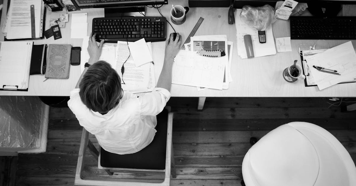 Black and white image of an employee working at a desk with papers and computer.