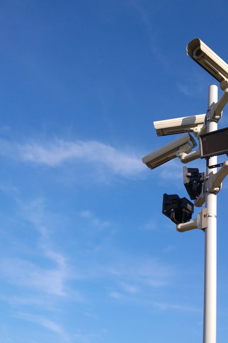 Multiple security cameras on a pole with a clear blue sky backdrop.