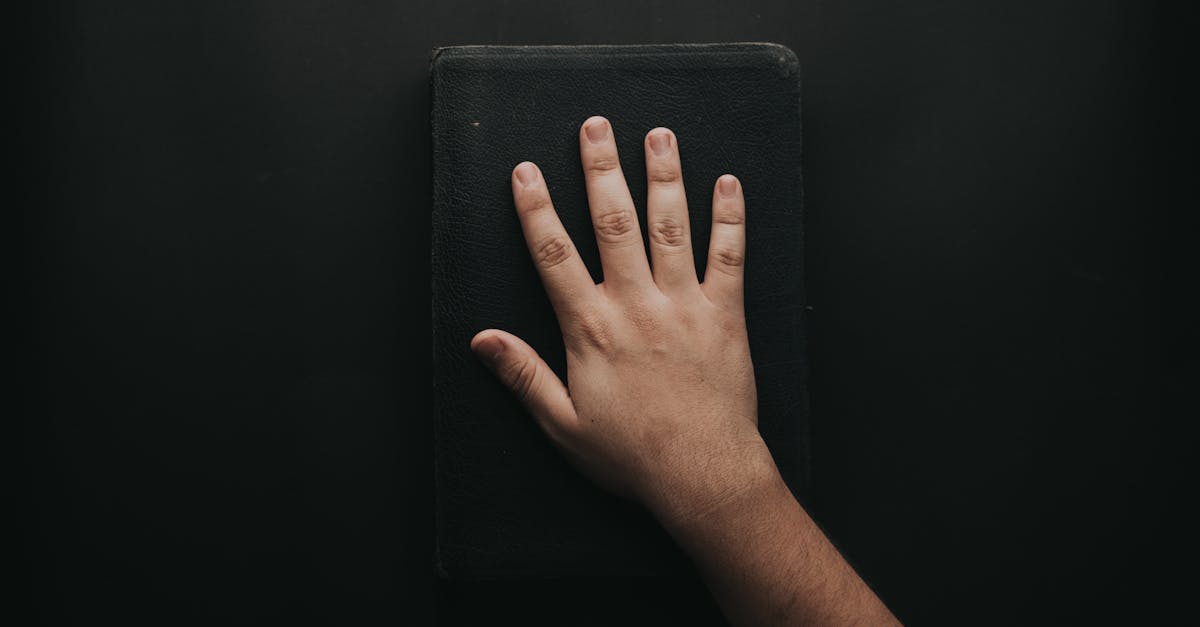 A close-up of a hand resting on a black book against a dark backdrop.