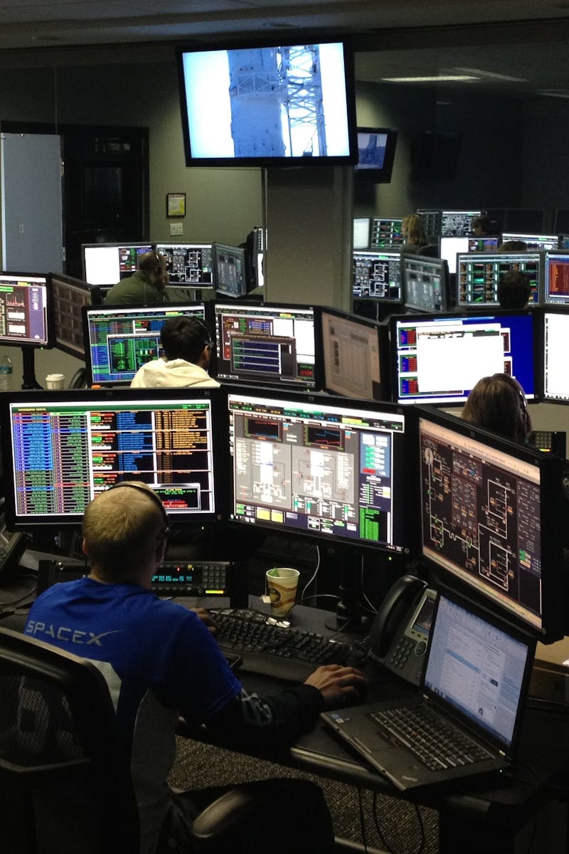 A bustling control room with people working on multiple computer monitors.