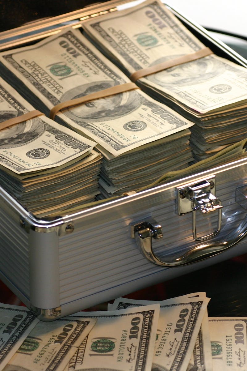 Open briefcase filled with stacks of hundred dollar bills on a glass table, representing wealth.