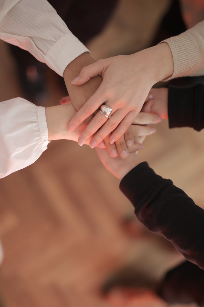 Top view of faceless friends in different clothes stacking hands together while standing on wooden floor indoor on sunny day