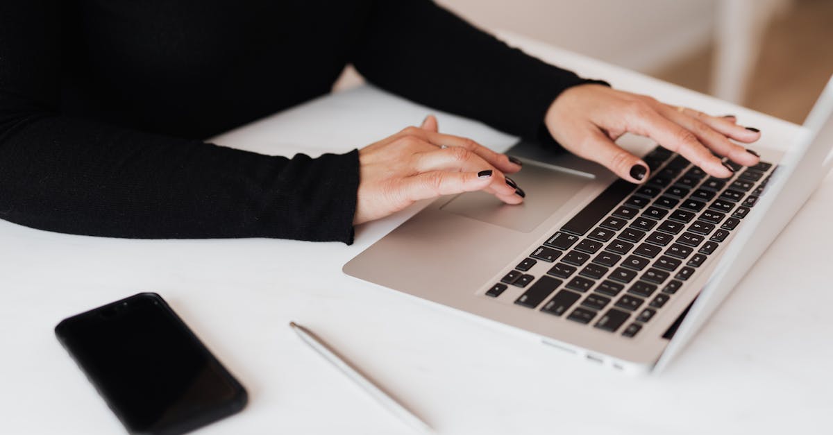 Professional woman typing on a laptop with smartphone and pen on desk, emphasizing modern business lifestyle.