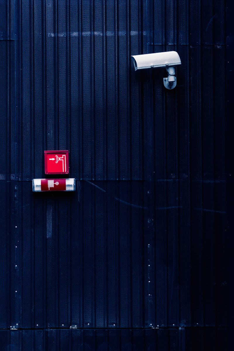 Modern security camera and exit sign on a corrugated metal wall, emphasizing surveillance and safety.