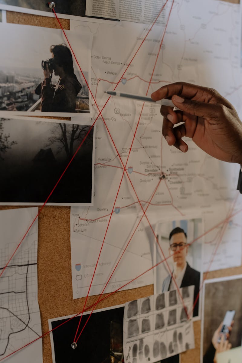 Detective examines a corkboard with maps and photos to solve a mystery.