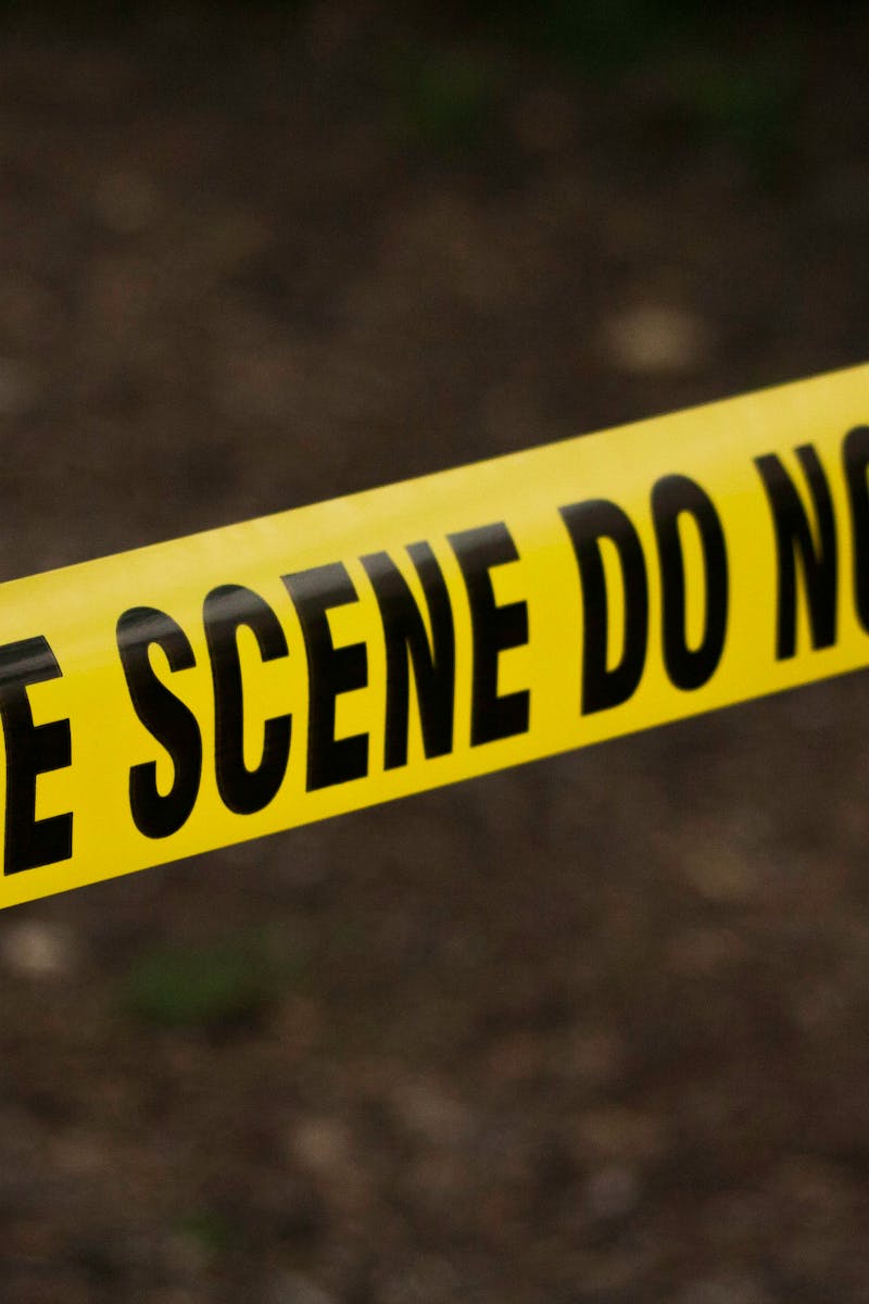 Close-up of crime scene tape with 'Do Not Cross' text, outdoors setting.