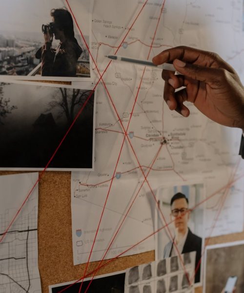 Detective examines a corkboard with maps and photos to solve a mystery.